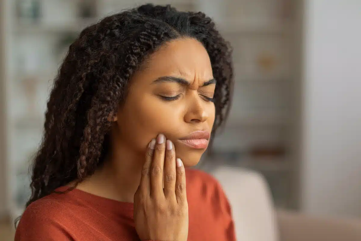 Woman wincing in pain while holding her jaw, indicating a dental emergency or toothache